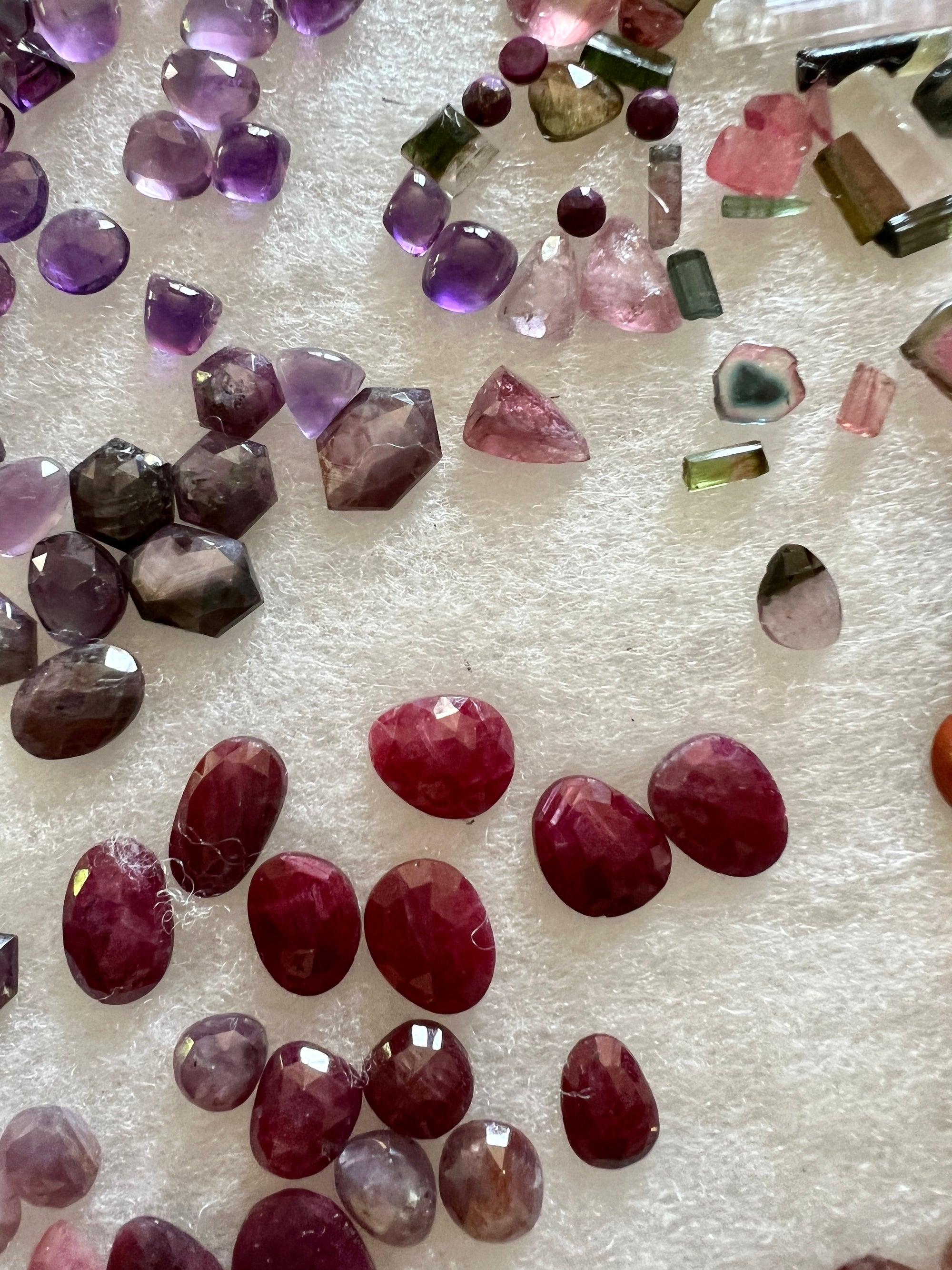 Ruby, garnet, watermelon tourmaline and amethyst cabochon stones lay in wait upon white fluffy material in a display case.