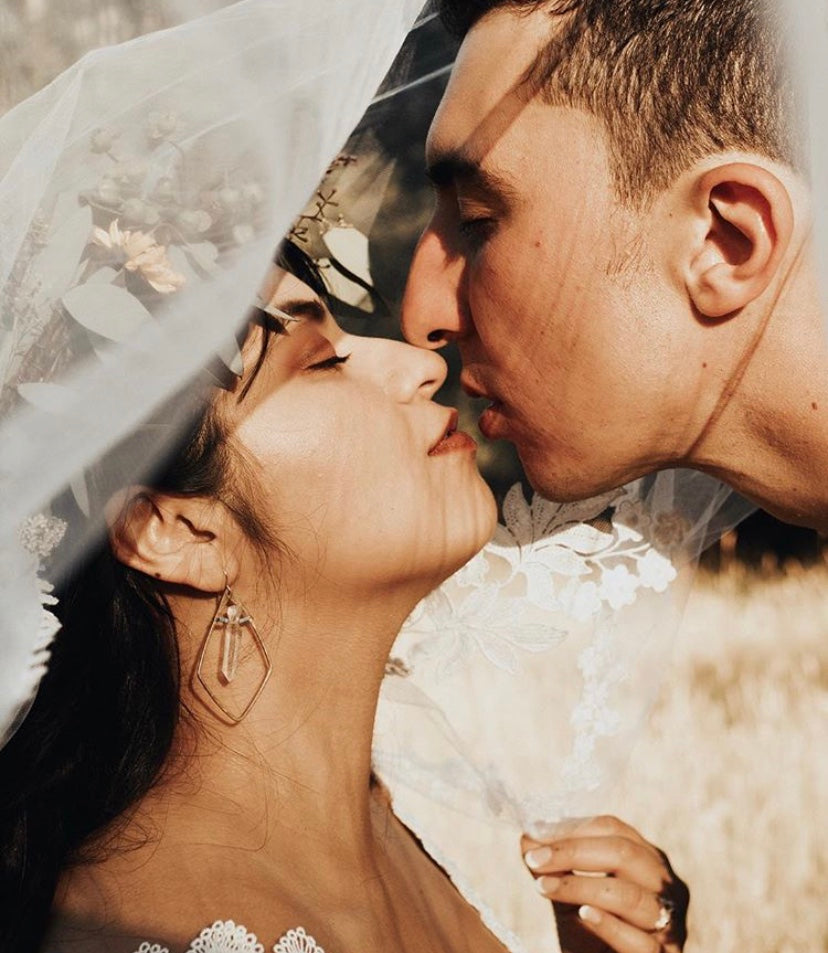 Sweet loving, newlyweds kiss. Beautiful Latino couple loving each other with woman wearing pigeon heart designs earrings beneath her bridal veil. We make bridal jewelry & jewelry as bridesmaid gifts & other wedding party presents.
