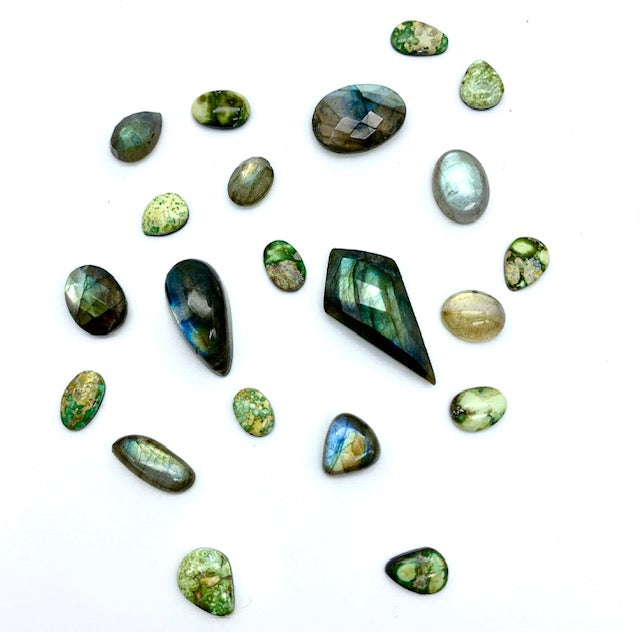 many different hues of greens, blues, and iridescent colored turquoise and labradorite stones of different shapes and sizes against a white background.